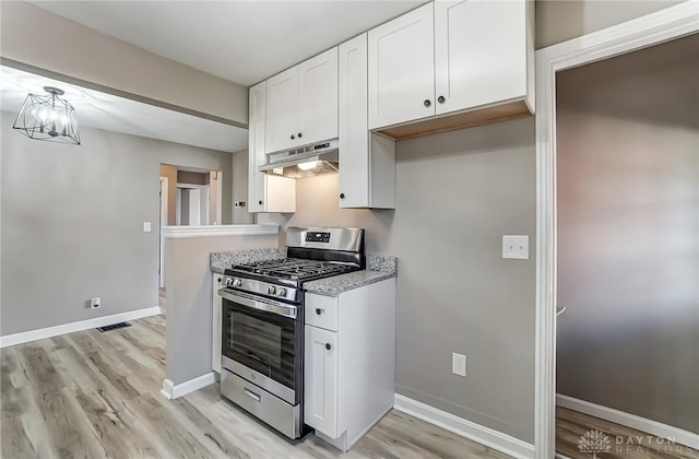 kitchen featuring stainless steel gas range, white cabinetry, under cabinet range hood, and baseboards