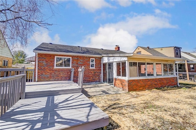 rear view of house featuring a deck, brick siding, fence, and a sunroom