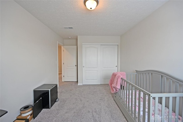 carpeted bedroom with a textured ceiling, visible vents, and a closet