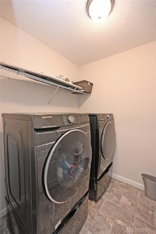 clothes washing area with laundry area, a textured ceiling, baseboards, and separate washer and dryer