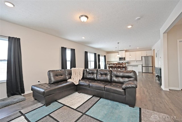 living area with recessed lighting, a textured ceiling, baseboards, and wood finished floors