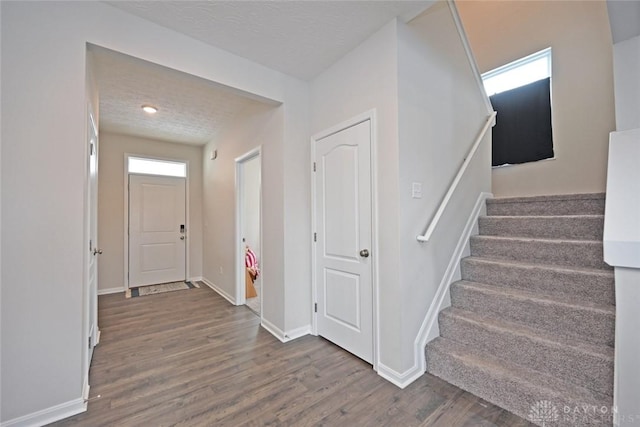 foyer with a textured ceiling, stairs, baseboards, and wood finished floors