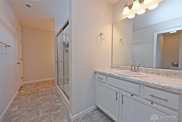 full bath featuring a textured ceiling, a stall shower, vanity, and baseboards