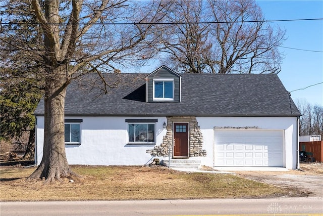 cape cod home featuring a shingled roof, driveway, an attached garage, and stucco siding