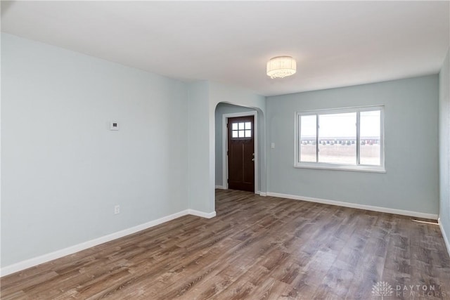 foyer entrance featuring arched walkways, baseboards, and wood finished floors