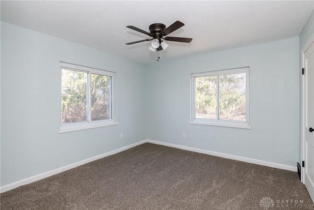 spare room featuring plenty of natural light, dark carpet, a ceiling fan, and baseboards