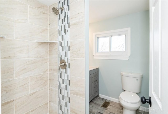 bathroom with toilet, tiled shower, vanity, and baseboards