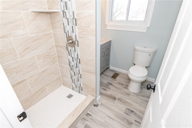 bathroom featuring toilet, wood finished floors, vanity, baseboards, and a stall shower