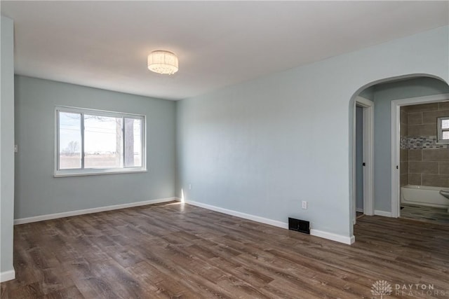 empty room featuring dark wood-type flooring, arched walkways, visible vents, and baseboards