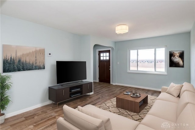 living room with arched walkways, baseboards, and wood finished floors