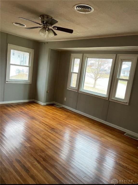 unfurnished room with a wealth of natural light, visible vents, and wood finished floors