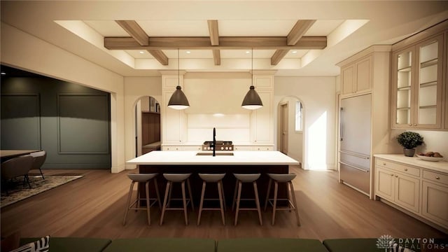 kitchen featuring arched walkways, wood finished floors, a kitchen breakfast bar, light countertops, and beam ceiling