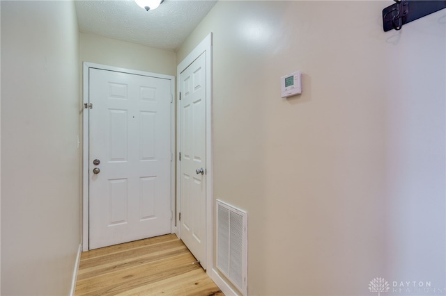 doorway with light wood finished floors, visible vents, and a textured ceiling