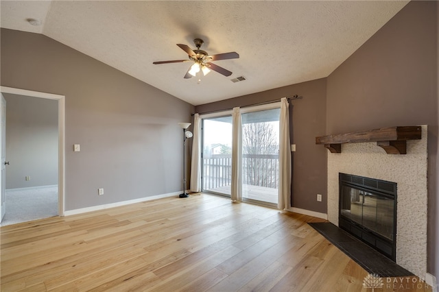 unfurnished living room featuring light wood finished floors, visible vents, a glass covered fireplace, vaulted ceiling, and baseboards