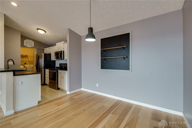 kitchen featuring stainless steel appliances, a sink, white cabinets, light wood finished floors, and dark countertops