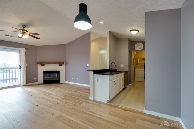 kitchen featuring washer / dryer, visible vents, a glass covered fireplace, light wood-style floors, and white cabinetry