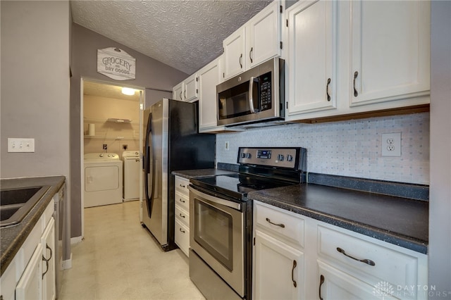 kitchen featuring stainless steel appliances, a sink, white cabinets, dark countertops, and washing machine and clothes dryer