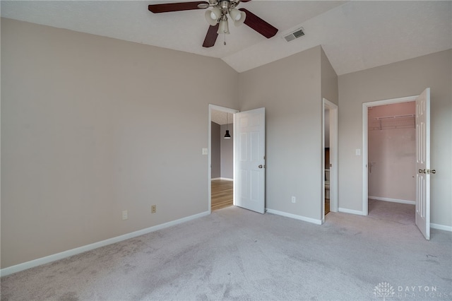 unfurnished bedroom featuring lofted ceiling, light carpet, visible vents, baseboards, and a walk in closet