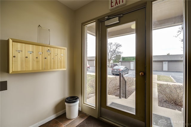 doorway to outside featuring mail area, baseboards, and dark tile patterned flooring