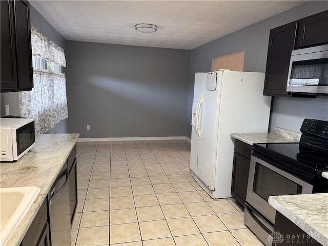 kitchen featuring light countertops, appliances with stainless steel finishes, light tile patterned flooring, a sink, and baseboards