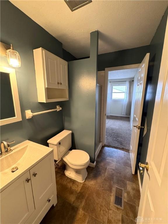 bathroom with toilet, a textured ceiling, vanity, and visible vents