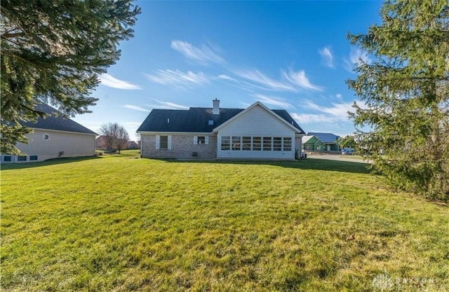 back of property featuring brick siding, a chimney, and a yard