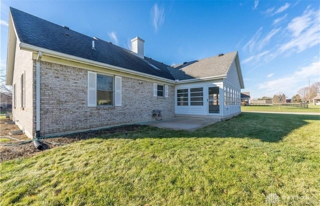 rear view of property with a patio, a yard, a shingled roof, a chimney, and brick siding