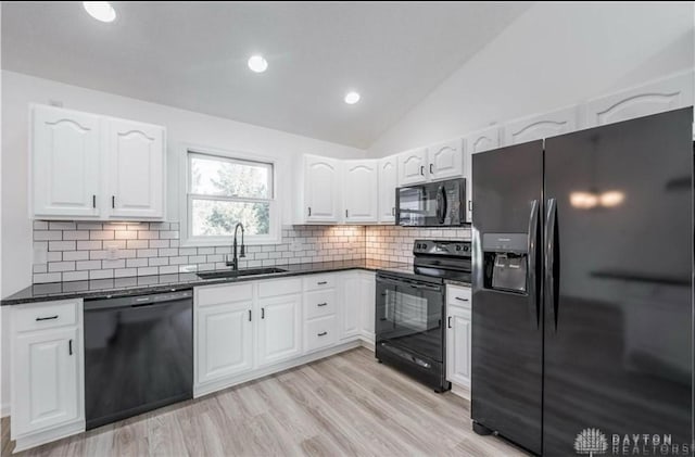 kitchen with lofted ceiling, a sink, black appliances, white cabinetry, and tasteful backsplash