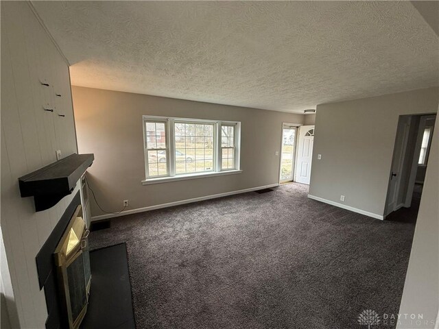 unfurnished living room featuring dark carpet, a textured ceiling, and baseboards