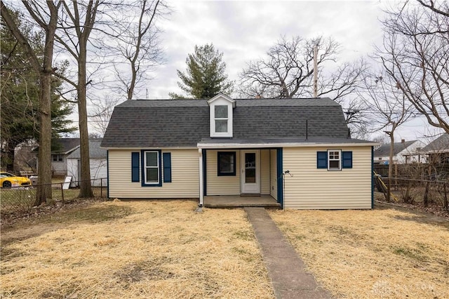 dutch colonial with covered porch, fence, a front lawn, and roof with shingles