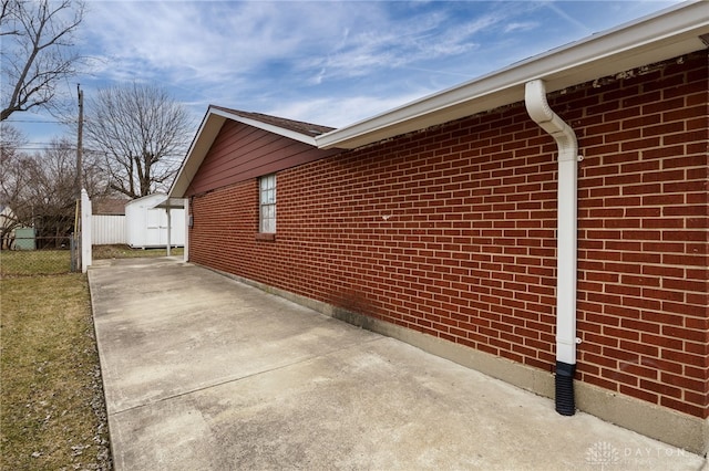 view of side of property featuring a storage shed, brick siding, an outdoor structure, and fence