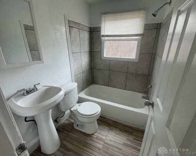 bathroom with washtub / shower combination, a textured wall, toilet, and wood finished floors