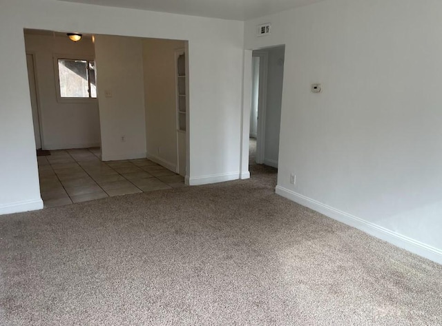 carpeted spare room with visible vents, baseboards, and tile patterned floors