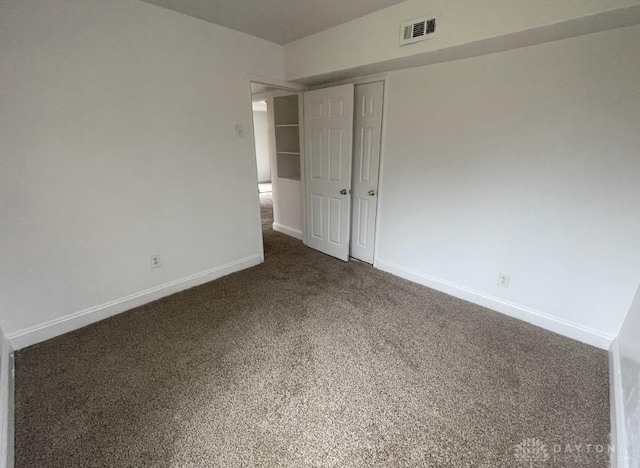 unfurnished bedroom featuring dark colored carpet, a closet, visible vents, and baseboards