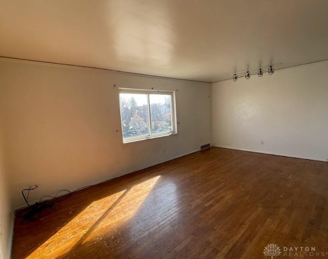 empty room with wood finished floors, visible vents, and track lighting