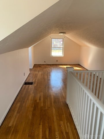 bonus room featuring visible vents, vaulted ceiling, a textured ceiling, wood finished floors, and baseboards