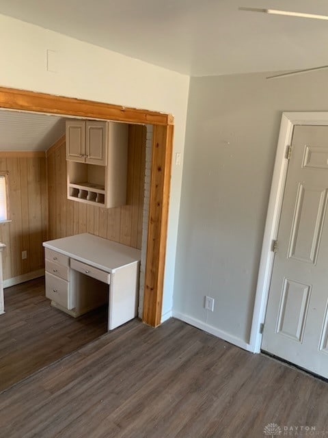 unfurnished office with baseboards, dark wood-type flooring, and wooden walls