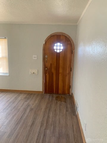 entryway featuring arched walkways, ornamental molding, a textured ceiling, and wood finished floors