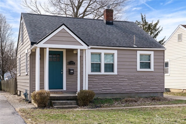 bungalow-style home with a shingled roof, stone siding, and a chimney