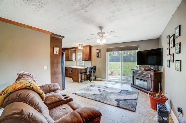 living room with a ceiling fan, a glass covered fireplace, a textured ceiling, and baseboards