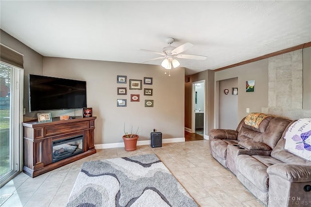 living room with light tile patterned floors, a glass covered fireplace, a ceiling fan, and baseboards