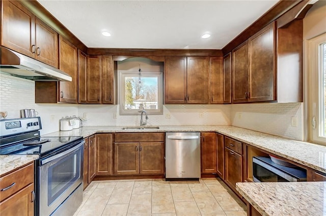 kitchen with under cabinet range hood, a sink, appliances with stainless steel finishes, backsplash, and light stone countertops