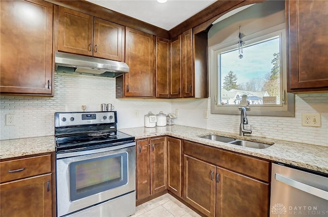 kitchen featuring light tile patterned floors, light stone countertops, stainless steel appliances, under cabinet range hood, and a sink