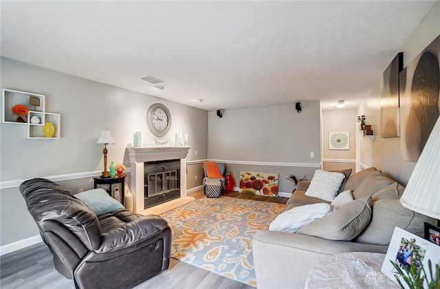 living area featuring a glass covered fireplace, wood finished floors, visible vents, and baseboards