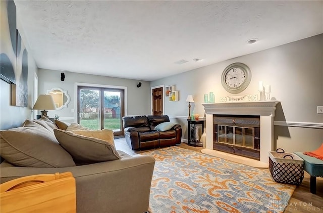 living room featuring a textured ceiling, baseboards, wood finished floors, and a glass covered fireplace