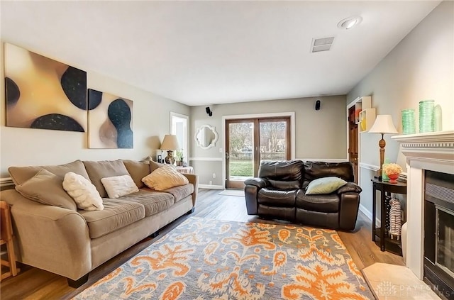 living room featuring visible vents, a fireplace, baseboards, and wood finished floors