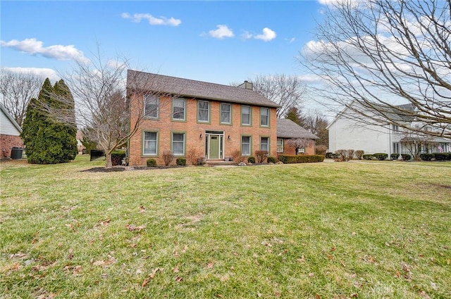 colonial house with a front yard, brick siding, a chimney, and central AC unit