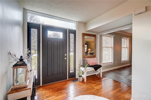 foyer entrance with light wood-style floors, baseboards, a wall of windows, and a textured ceiling