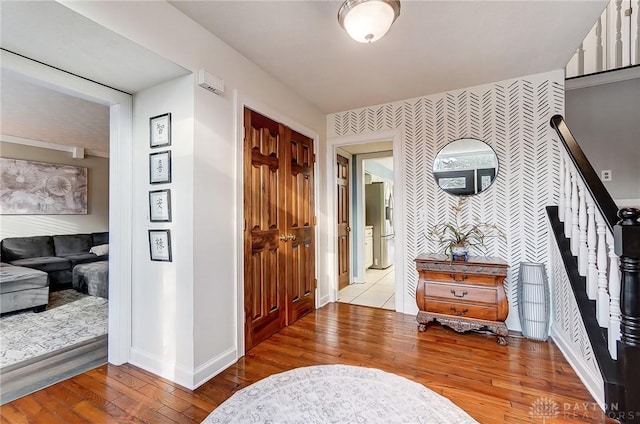 foyer with an accent wall, baseboards, stairway, wood-type flooring, and wallpapered walls