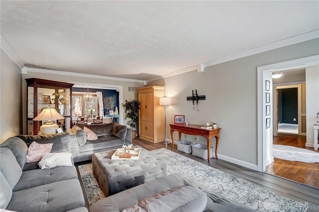 living area featuring crown molding, an inviting chandelier, wood finished floors, and baseboards